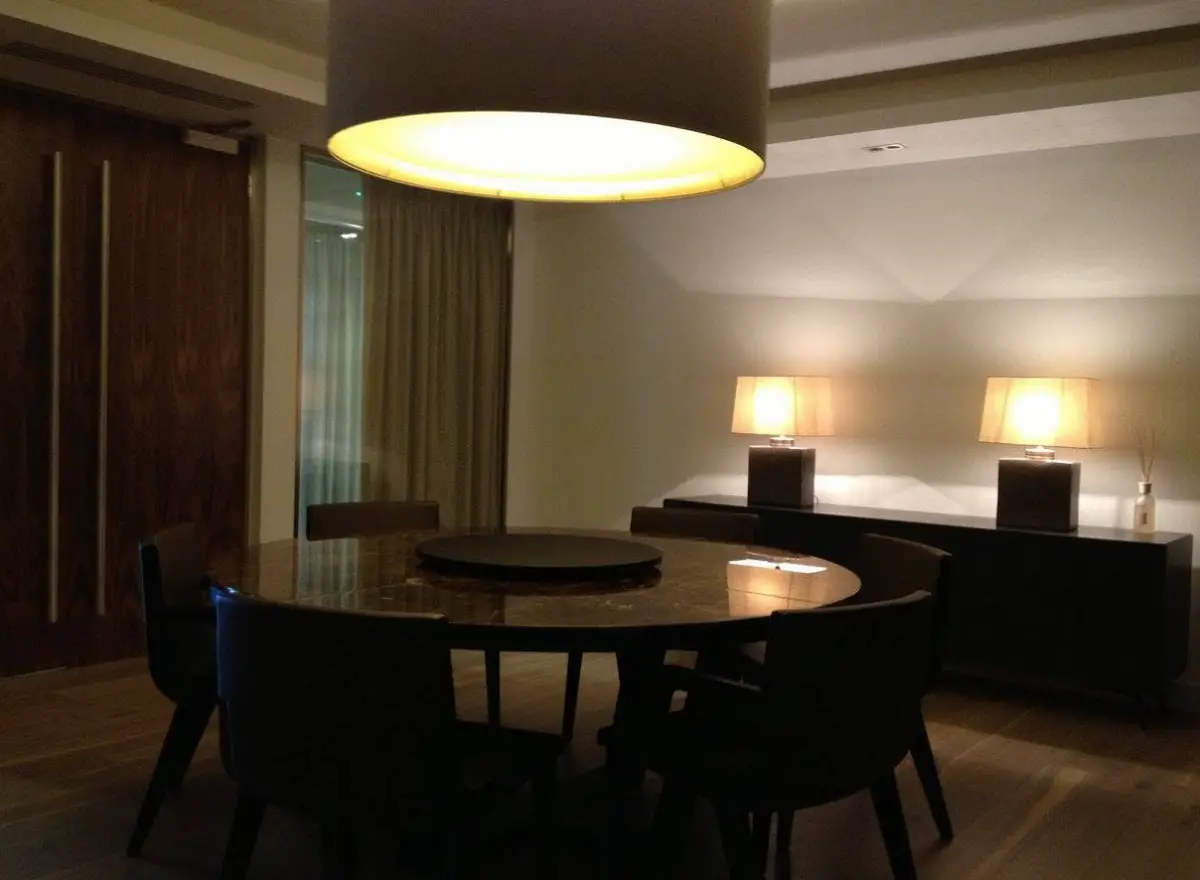 Round dining table under large warm circular pendant light fixture